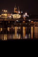 .panoramic view of Prague Castle and St. Vitus Cathedral and the Vltava River and street lights on bridges at night in the center of Prague