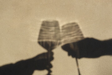 Shadow on the wall of hands of a romantic couple toasting with two glasses of wine. Cheers, cincin