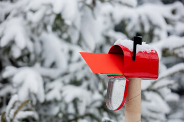 Red envelope in mailbox in a snow near pine tree in winter