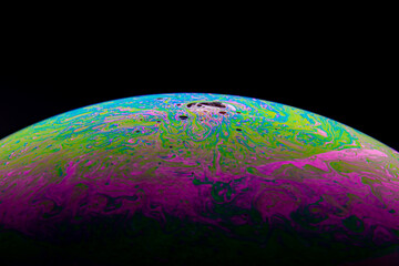 Close up, macro shot of a rainbow, multi colored soap bubble with yellow, purple, pink, blue and green colors on black background. 