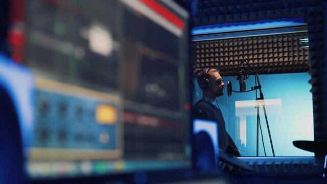 Male Rap Singer with Headphones and Sound Engineer are Creating a New Song in Professional Recording Studio. Program and Tools for Creating Music on Computer Monitor. Work in the Music Recording Room