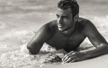 Sexy handsome topless male model enjoying the ocean water on the beach. Black and white. 