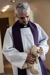 Catholic priest holding child plush toy teddy bear