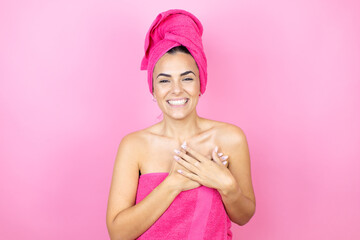 Young beautiful woman wearing shower towel after bath standing over isolated pink background smiling with her hands on her chest and grateful gesture on her face.