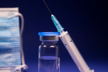 Vaccine bottle phial with no label near blue medical mask and medical syringe with injection needle. isolated on blue background. cure. Development of coronavirus vaccine COVID-19.