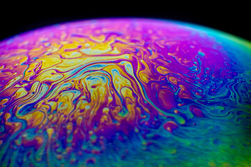 Close up, macro shot of a rainbow, multi colored soap bubble with yellow, purple, pink, blue and green colors on black background. 