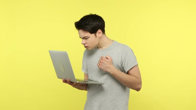 Young man student in gray t-shirt typing on laptop, working on information technology project, creating program, developing web site, creativity. Indoor studio shot isolated on yellow background