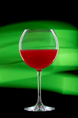 glass cocktail glass with red liquid on black background. Green light in the background.