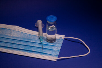 Vaccine bottle phial with no label on blue medical mask and medical syringe with injection needle....