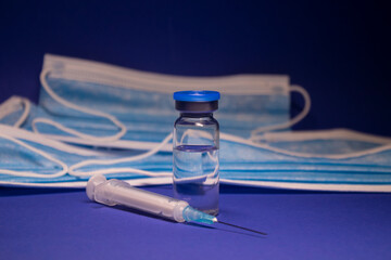 Vaccine bottle phial with no label and medical syringe with injection needle on background of blue...