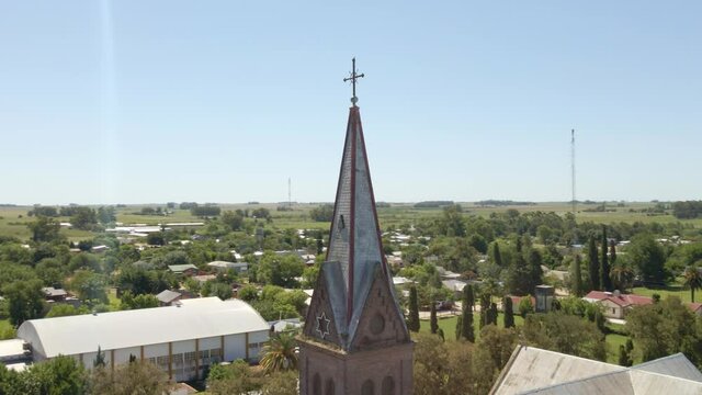 Orbital close up of a romantic style church tower and cross with Santa Anita town and Entre Rios countryside in background, Argentina