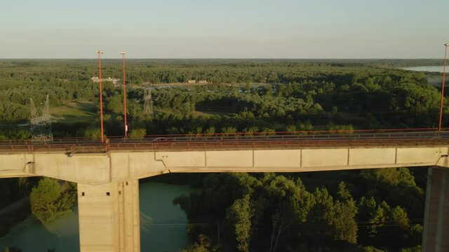 Dolly right flying alongside road and railway complex cable-stayed bridge with large green field, forest area and river at golden hour