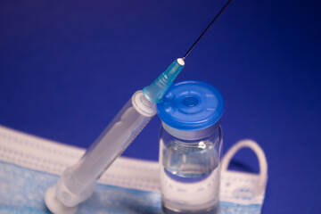 Vaccine bottle phial with no label on blue medical mask and medical syringe with injection needle....