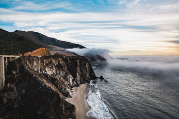 Scenic view of ocean shore near Big Sur, California, USA. Cloud covered coast, sea and cliff hills. Foggy pink sunset landscape.