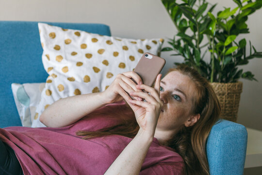 Young woman looks into the smartphone screen while lying on the couch. FOMO - Fear Of Missing Out