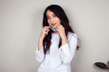 young asian woman doctor in white uniform gesturing positive on gray background, wearing a mask, lifestyle healthcare people concept
