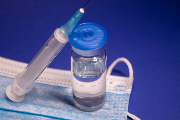 Vaccine bottle phial with no label on blue medical mask and medical syringe with injection needle. isolated on blue background. cure. Development of coronavirus vaccine COVID-19.