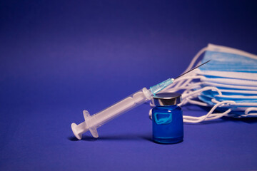 Vaccine bottle phial with no label and medical syringe with injection needle near pile of blue...