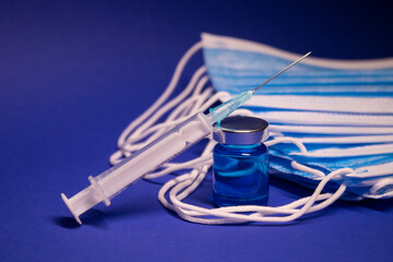 Vaccine bottle phial with no label and medical syringe with injection needle near pile of blue...