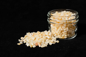 Broken white corn seeds in a glass jar on a black surface. 45 deg. view,