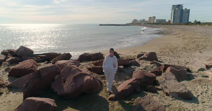 Mujer adlib con mascarilla covid-19 paseando entre rocas del mediterr&aacute;neo