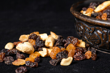 Mix of energetic seeds and dried fruits in a wooden bowl on a black surface. Close up.