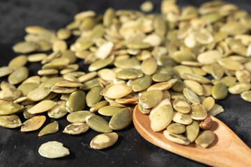 Isolated stack of toasted hulled pumpkin seeds on black background seen from atop, some seems are displaced around the stack
