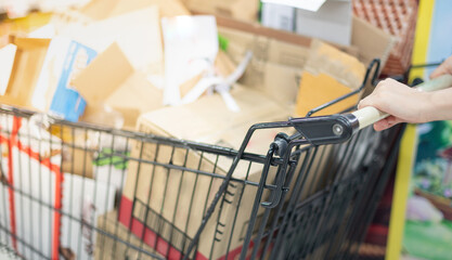 Blurred effect of  female worker hands pushing pile of used cardboard packaging boxes in the Supermarket aisle with silver and black shopping trolley and waiting for for recycle process.