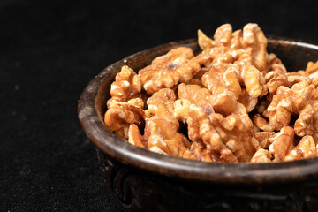 Carved wooden bowl with peeled walnut seeds on a black background.