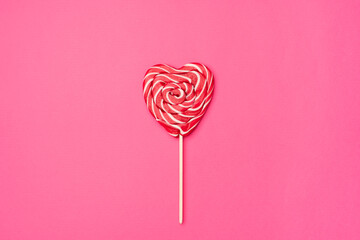 Red heart-shaped lollipop candy isolated on an empty colorful pink background. Symbol of love for...