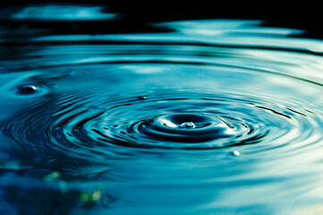 Circular waves and ripples in the water from a drop falling. Natural background blue water with...