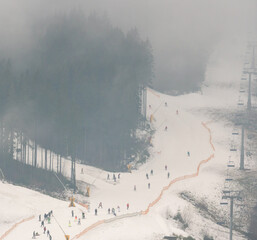 Skiing in the Fog Aerial View. Misty Low Season in Bukovel, the largest ski resort in Ukraine Carpathian Mountains. Slopes covered With Man-Made Snow at Warm Autumn Weather