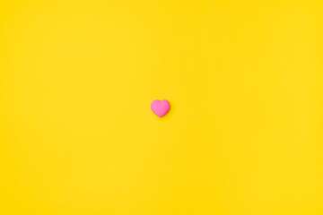 Pink heart isolated in the center on an empty colorful yellow background. Symbol of love for Happy Women's, Mother's, Valentine's Day, Birthday greeting romantic postcard. Flat lay, top view, copy