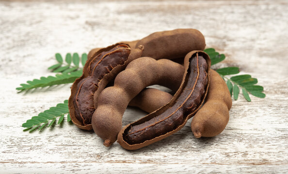 Tamarind fruits with green leaves on wood background.
