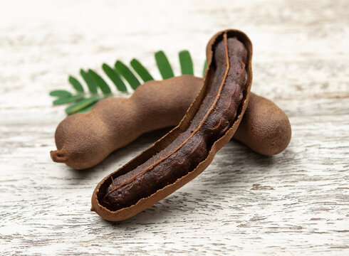 Tamarind fruits with green leaves on wood background.