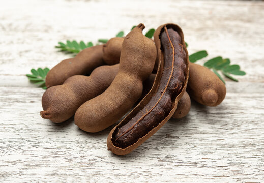 Tamarind fruits with green leaves on wood background.