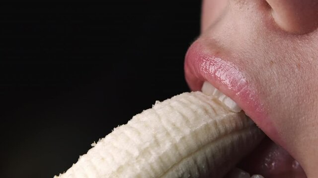 Sexy young woman seductively bites and eating fresh banana. Close-up view of female mouth, sensual footage. Slow motion.