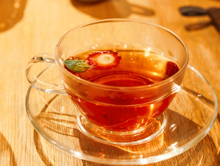 Transparent teacup with strawberry tea and a single strawberry slice floating on top