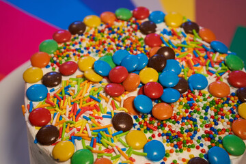 Fototapeta na wymiar Cake of sponge cake and cream covered with multicolored candies. rainbow background.