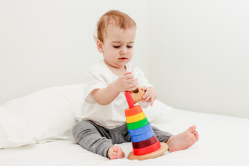 Cute baby boy playing colorful pyramid tower on white bed