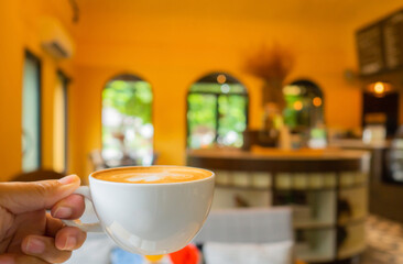 beautiful shape foam cappuccino coffee cup in man hand holding up in yellow classic background with copy space