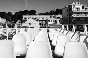 Upper deck of a ferry filled with white empty seats; in the background a seaside town
