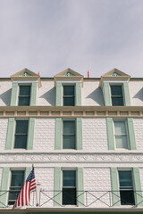 Facade of an old building; white brick with mint green shutters; American flag flying