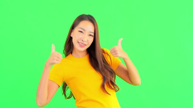 A young woman against a solid green background smiles as she gives the thumbs up for success.