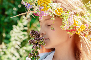 Portrait of a happy cute pretty girl in a wreath of wildflowers. Summer bright sunlight. Happy childhood concept. Positive emotions. Close-up