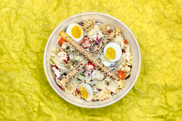 High-angle view of a Mediterranean salad with pasta, eggs, vegetables adn breadsticks.