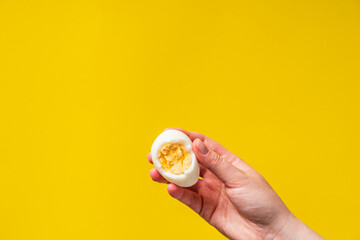 Fototapeta na wymiar Close up on hand holding boiled egg with yolk in front of yellow background