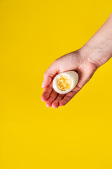 Fototapeta na wymiar Close up on hand holding boiled egg with yolk in front of yellow background