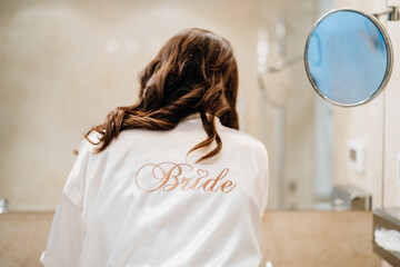 Wedding day preparation.Bride wearing a white bridal bathrobe doing makeup and...
