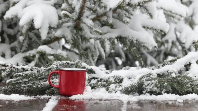 Red cup of coffee and snow around on wooden table in blizzard